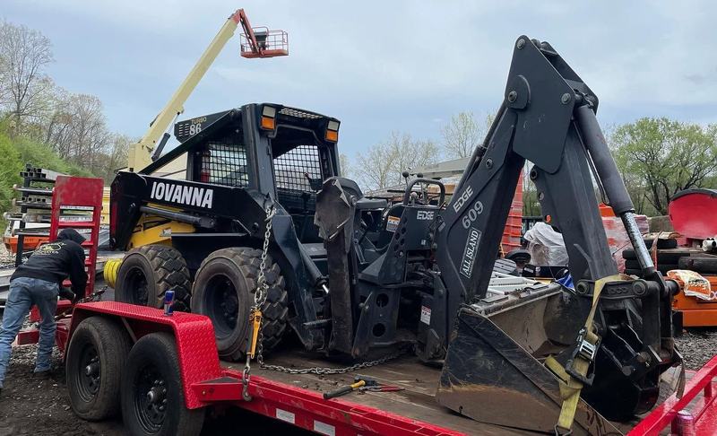 Iovanna skid steer with a backhoe attachment on a trailer